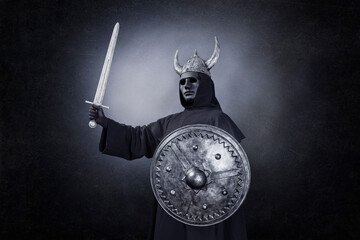 Scary figure with horned helmet, sword and round shield in the dark