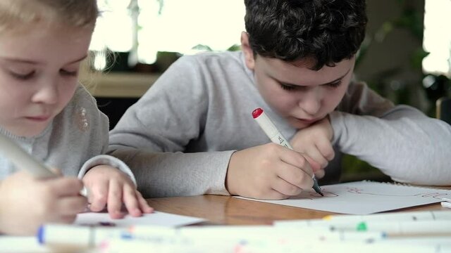 Children draw pictures with a colored pencil on paper in bright living room using their imagination, creates art home, dreaming of becoming an artist. Teaching children to draw at school and at home.
