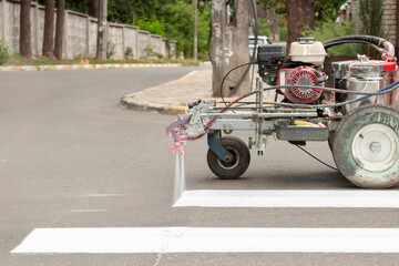 City workers paint crosswalk lanes on the road with painting machine.