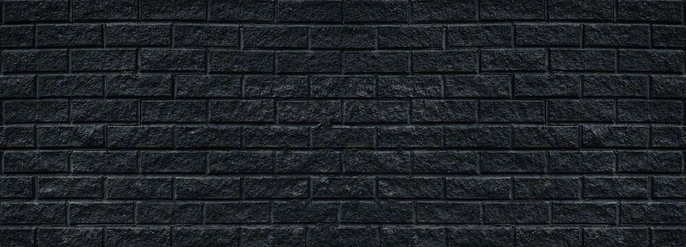 Wide old black shabby brick wall texture. Cracked masonry panorama. Dark rough brickwork grunge background