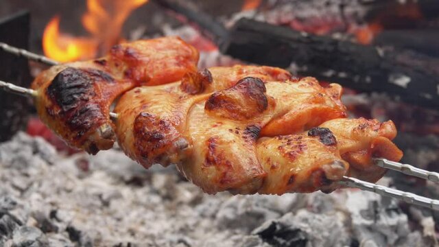 Mouth-watering chicken wings on the skewers are flipped above the open fire outdoors in rapid 