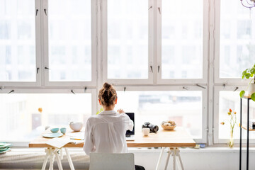 Rear view of young woman working on laptop in loft office
