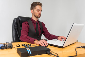 young handsome man with a beard in a bright room sitting at a table, working, on the table are...