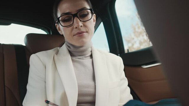 A concentrated young businesswoman is working with papers sitting in the car 