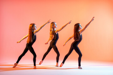 group of three girls in black tight-fitting suits dancing on red background with their long hair down.