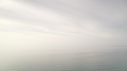 Clouds over calm sea water, misty foggy weather. Haze over horizon.