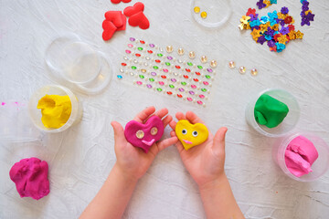 Child playing with colorful modeling clay with  beads and sequins and sculpting heart figure. Home Education game with clay. Early development concept