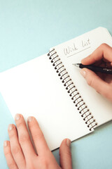 Woman's hand holding pen and open spiral notebook with blank white pages on light background. Wish list