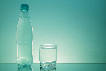 A bottle of water and a glass cup are on a mirrored table. Sparkling water . Plastic bottle. Gas bubbles in water.