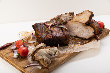 Meat baked in the oven, on a board covered with baking paper, with slices of black bread, with chopped red onion, hot pepper, tomatoes, rosemary, on a light background
