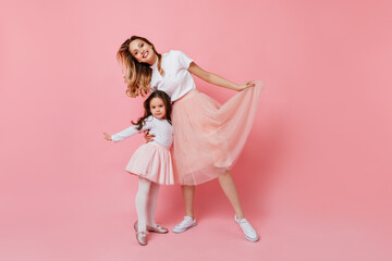 Portrait of beautiful young mother and her little daughter in identical romantic outfit smiling on pink background