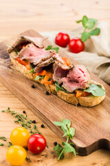 Bruschetta with roast beef, fresh herbs and paprika on a board on a light wooden background.