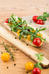 Bruschetta with mozzarella, cherry tomatoes and arugula with olive oil on a board on a light wooden background.