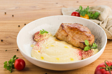 Pork steak with mashed potatoes in a plate on a light wooden background.