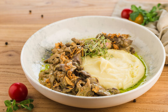 Beef stroganoff with mashed potatoes in a plate on a light wooden background.