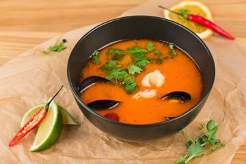 Tom yam soup with shrimp and mussels in a bowl on a light wooden background close-up.