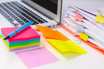 Close-up of a pile of papers with a post-notebook, colored post its and a pen. Information overload concept