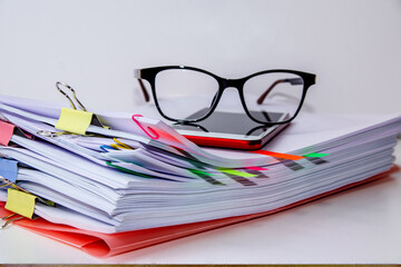 Close-up of glasses and a smartphone on a pile of folios. Information overload concept