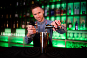 Young guy working as a bartender preparing cocktails in a pub