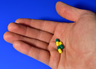 Pills in capsules in hand on blue background. Medicine grade pharmaceutical tablets. Medical pill for maintaining and improving health. Antidepressant addiction and depression concept