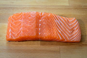A big piece of fresh raw salmon fillet meat which is placed on wooden cutting board, preparation for cooking. 