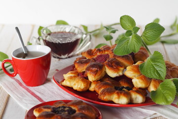 Food background.Beautiful yeast buns in the form of flowers for tea, in a red plate on a light background with sprigs of mint.