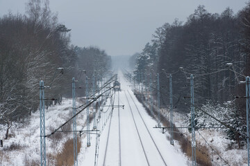 Dwutorowy szlak kolejowy zimą z przejeżdżającą lokomotywą elektryczną.