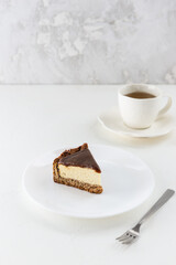Slice of tofu cheesecake with salted caramel on a white plate with a cup of tea. Vegan dessert, sugar, gluten and lactose free.