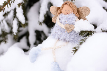 A soft textile doll with golden heart in hands sitting on the snow. Valentine’s Day, love, Merry Christmas, New Year concept.