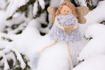 A soft textile doll with golden heart in hands sitting on the snow. Valentine’s Day, love, Merry Christmas, New Year concept.