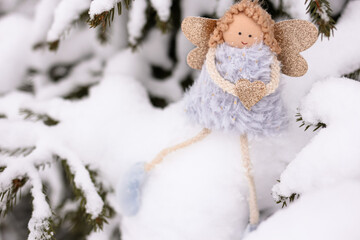 A soft textile doll with golden heart in hands sitting on the snow. Valentine’s Day, love, Merry Christmas, New Year concept.
