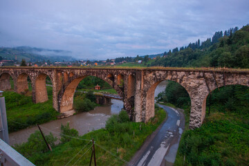 Fototapeta na wymiar Arched old brick railway bridge in the picturesque mountains among the forest of meadows tourist trail Carpathians