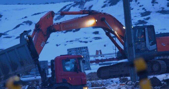 Earthwork at a construction site in winter, an excavator digs a place for a foundation, in the distance an excavator with a ripper tooth performs overburden works, softening the frozen soil