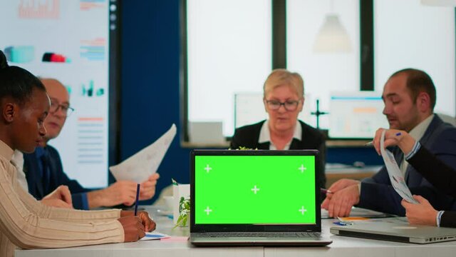 Group of business people discussing company plan with mockup laptop in front of camera, pc ready for financial project presentation placed on desk. Leader using green screen pc with chroma key display