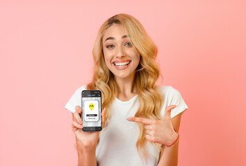 Happy woman pointing at smartphone with mobile taxi app on screen over pink studio background. Urban transport concept