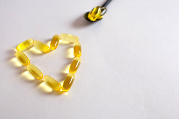 fish oil in capsules on a white background in the shape of a heart. Spoon fish oil capsules. A useful food supplement for good heart function. Useful animal fats omega-3, omega-6 for the human body