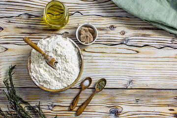 Ingredients for making Dough for focaccia or pizza. Flour, olive oil, yeast, seasonings, salt, herbs, greens close-up on a wooden table, copy space
