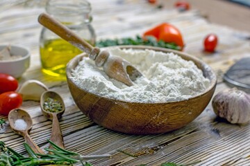 Ingredients for making Italian focaccia bread. Flour, olive oil, yeast, seasonings, salt, tomatoes, sweet herbs, greens close-up on a wooden table, copy space