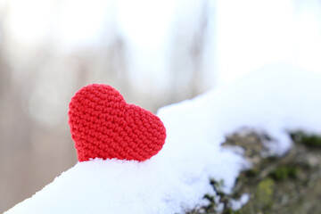 Fototapeta premium Valentine heart on the snow in sunlight. Red knitted symbol of romantic love on a branch in winter forest, background for holiday