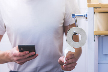 Pastime on the toilet: Young man using his smartphone while sitting on the toilet