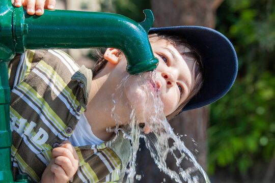 Kind trinkt Wasser aus Pumpbrunnen