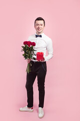 Valentines day. Handsome smiing boy holding flowers and gift box on pink background.