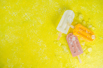 Selection of bright multicolored ice cream popsicle. Various gelato, frozen lollypops - chocolate vanilla blueberry strawberry pistachio orange, with crushed ice on trendy yellow sunny background