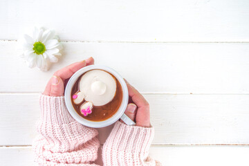 Easter hot chocolate with marshmallow bunny rabbits. Girl hands hold cup with funny hot cocoa drink, wooden background copy space top view