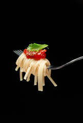 Pasta with tomato sauce on a fork with green leaf lettuce. Delicious Italian spaghetti pasta with pesto sauce. Image minimalism and dark background