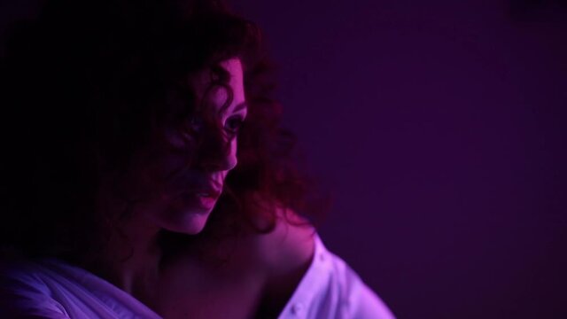 Fashion model curly woman in neon lights posing, light reflections on the skin