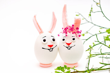 Happy Easter concept.Creative Easter bunnies made of eggs with funny faces painted on them.White background,fresh flowers.Copy space for text.