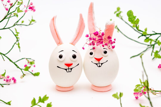 Creative Easter bunnies made of eggs with funny faces painted on them.White background,fresh flowers.Happy Easter concept.