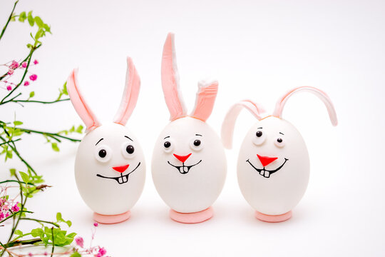 Happy Easter concept.Creative Easter bunnies made of eggs with funny faces painted on them.White background,fresh flowers.