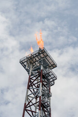 Obraz premium Flare torch on a tower burning excess gas from an oil production platorm at offshore oil field